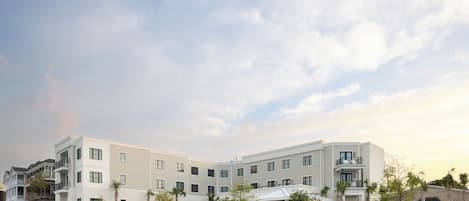 A multi-story hotel with a modern design, featuring balconies, a pool area, and a landscaped garden.