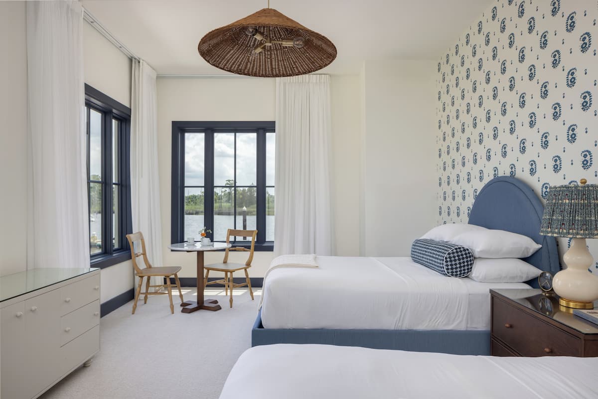 A bedroom with two beds, a desk, chairs, a dresser, and a large window.
