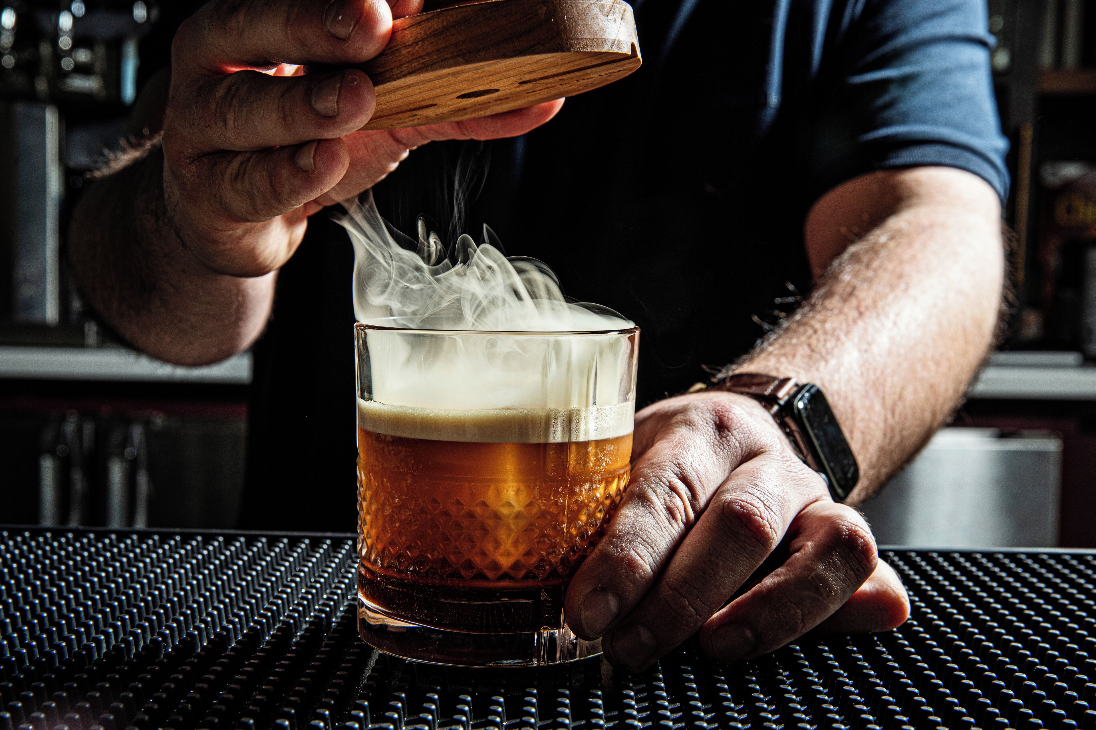 A person pouring a drink into a glass, with a bar setting in the background.
