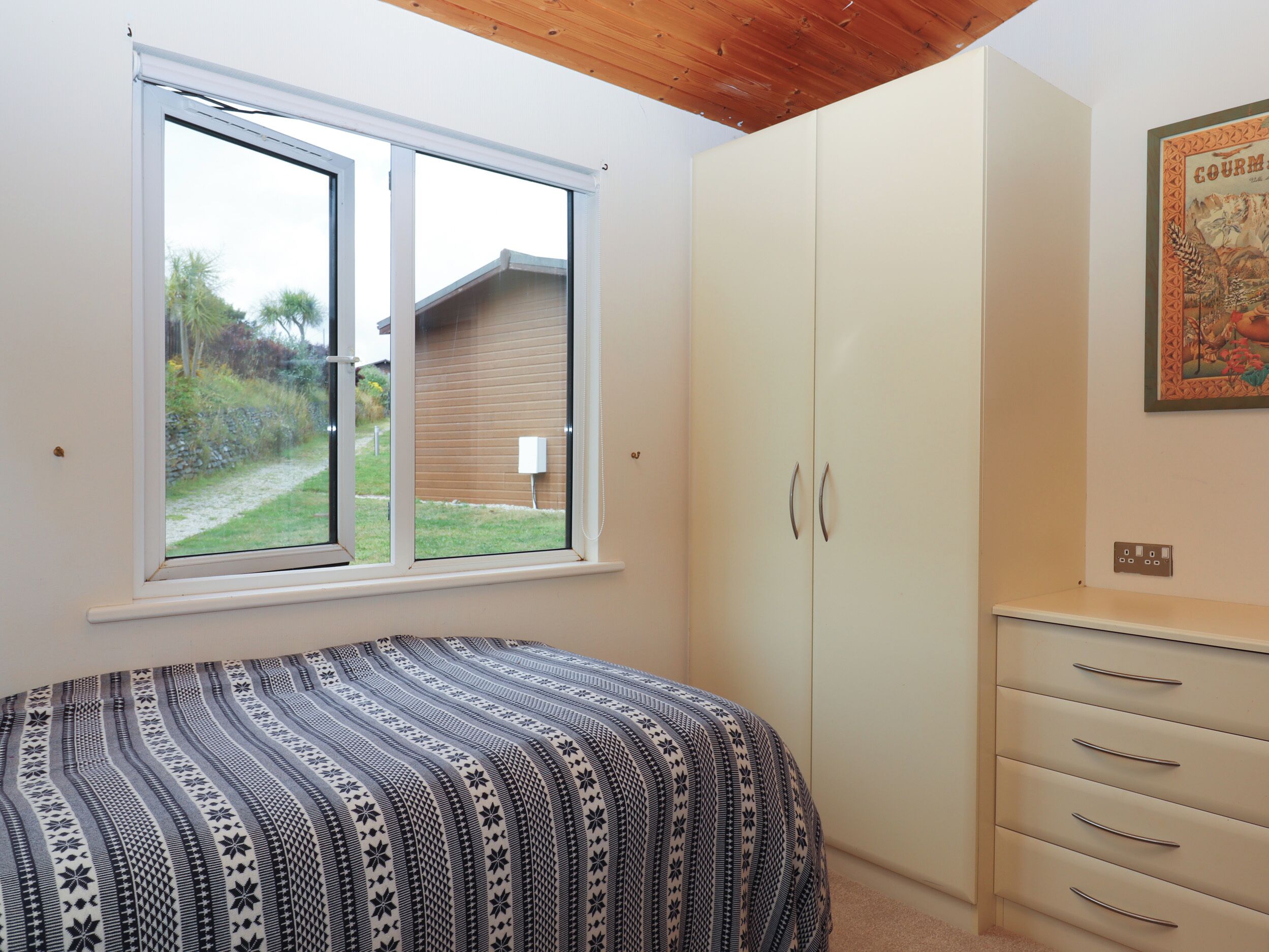 A bedroom with a bed, a wardrobe, a window, and a painting on the wall.