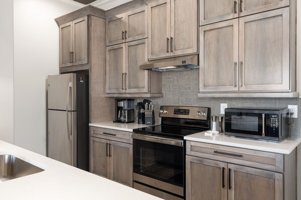 Una cocina moderna con electrodomésticos de acero inoxidable, armarios de madera y una encimera blanca.