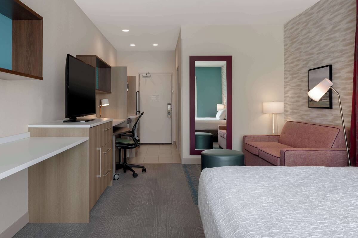 Hotelkamer met een bed, bureau met een computer, televisie, bank en een badkamer zichtbaar door een geopende deur.