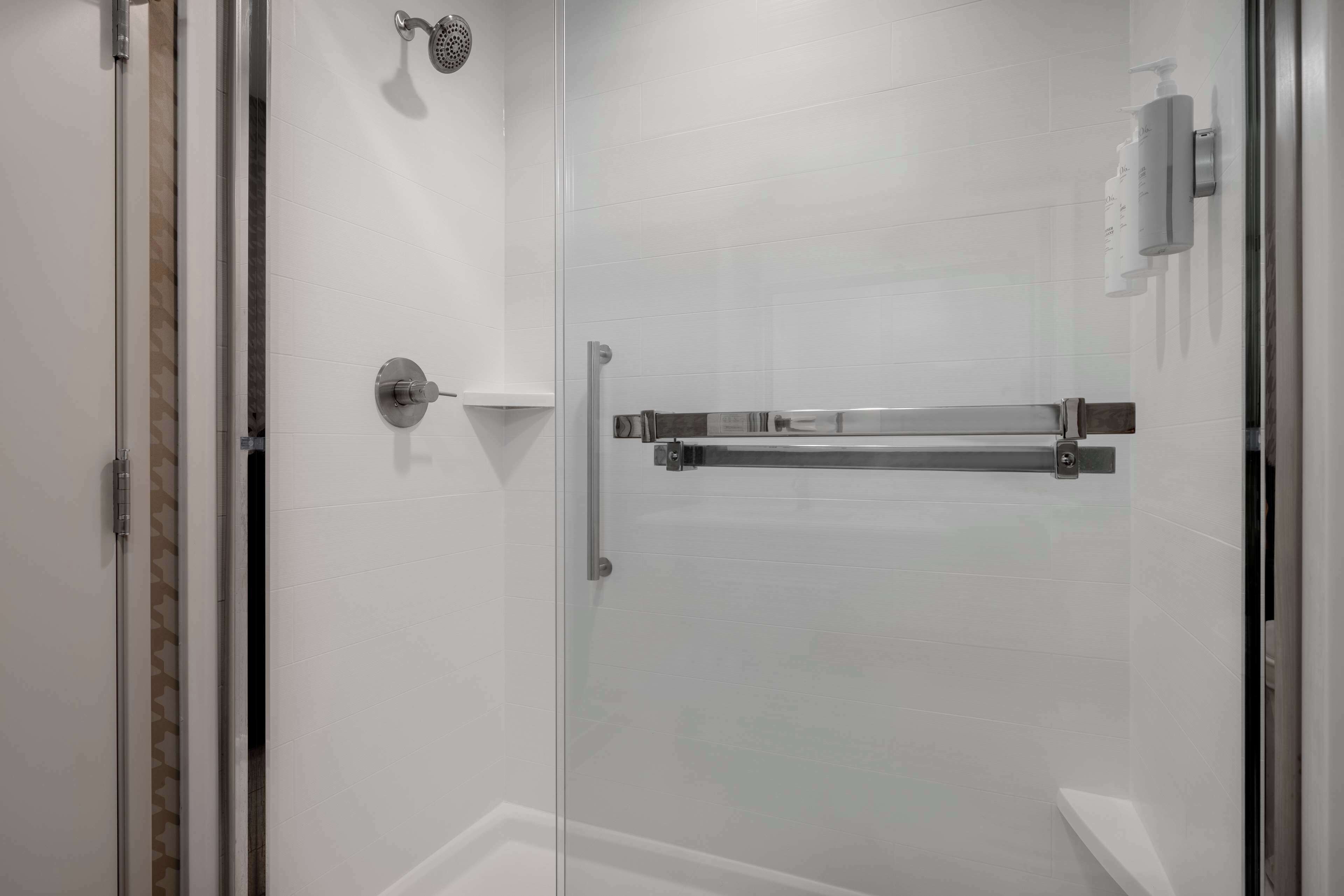 A glass-enclosed shower area with a showerhead, a towel rack, and a soap dispenser.