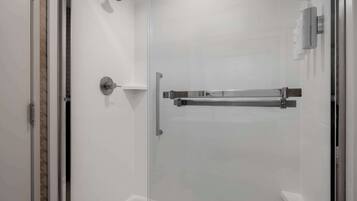 A glass-enclosed shower area with a showerhead, a towel rack, and a soap dispenser.
