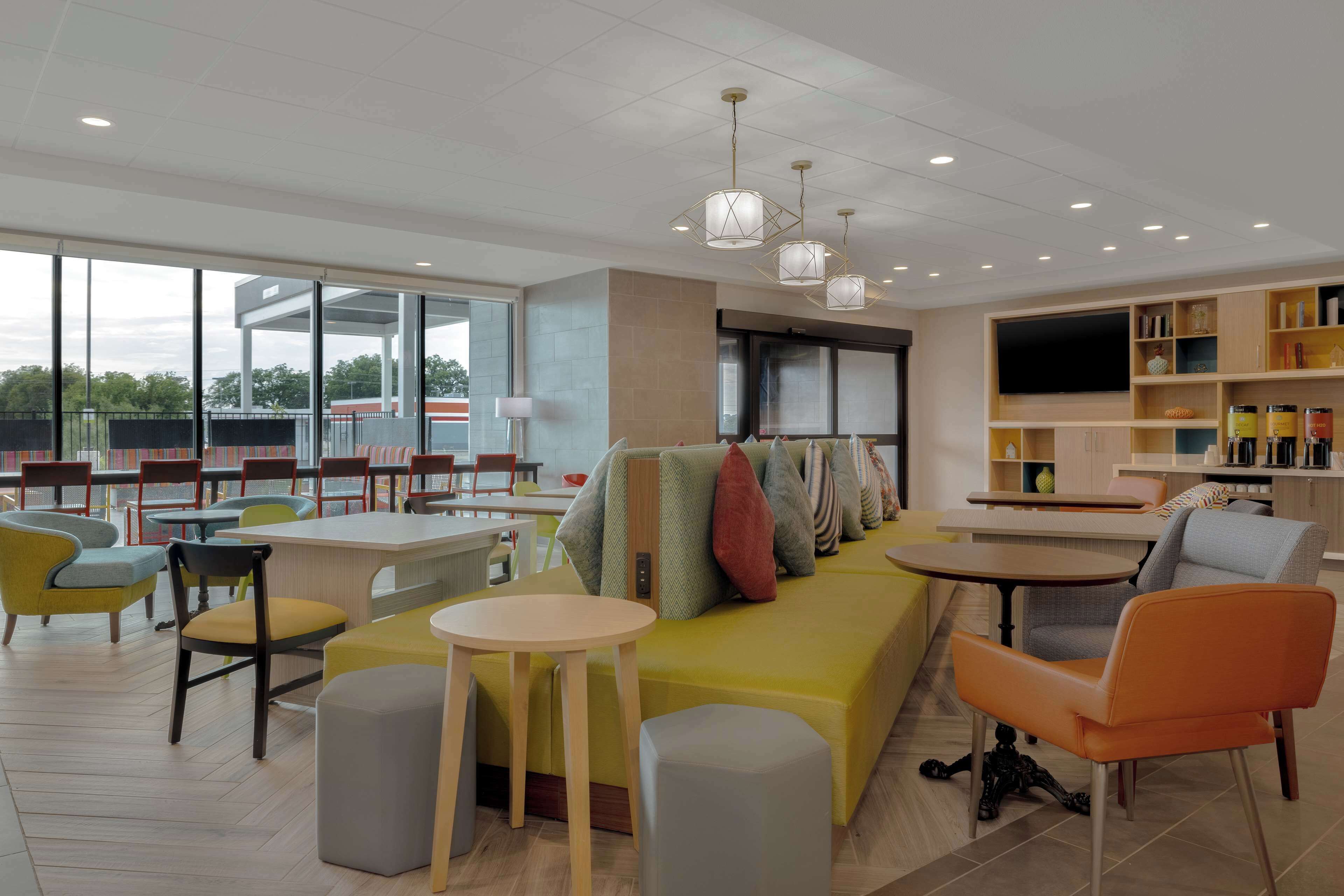 A modern hotel lobby with a sofa, chairs, tables, and a TV.