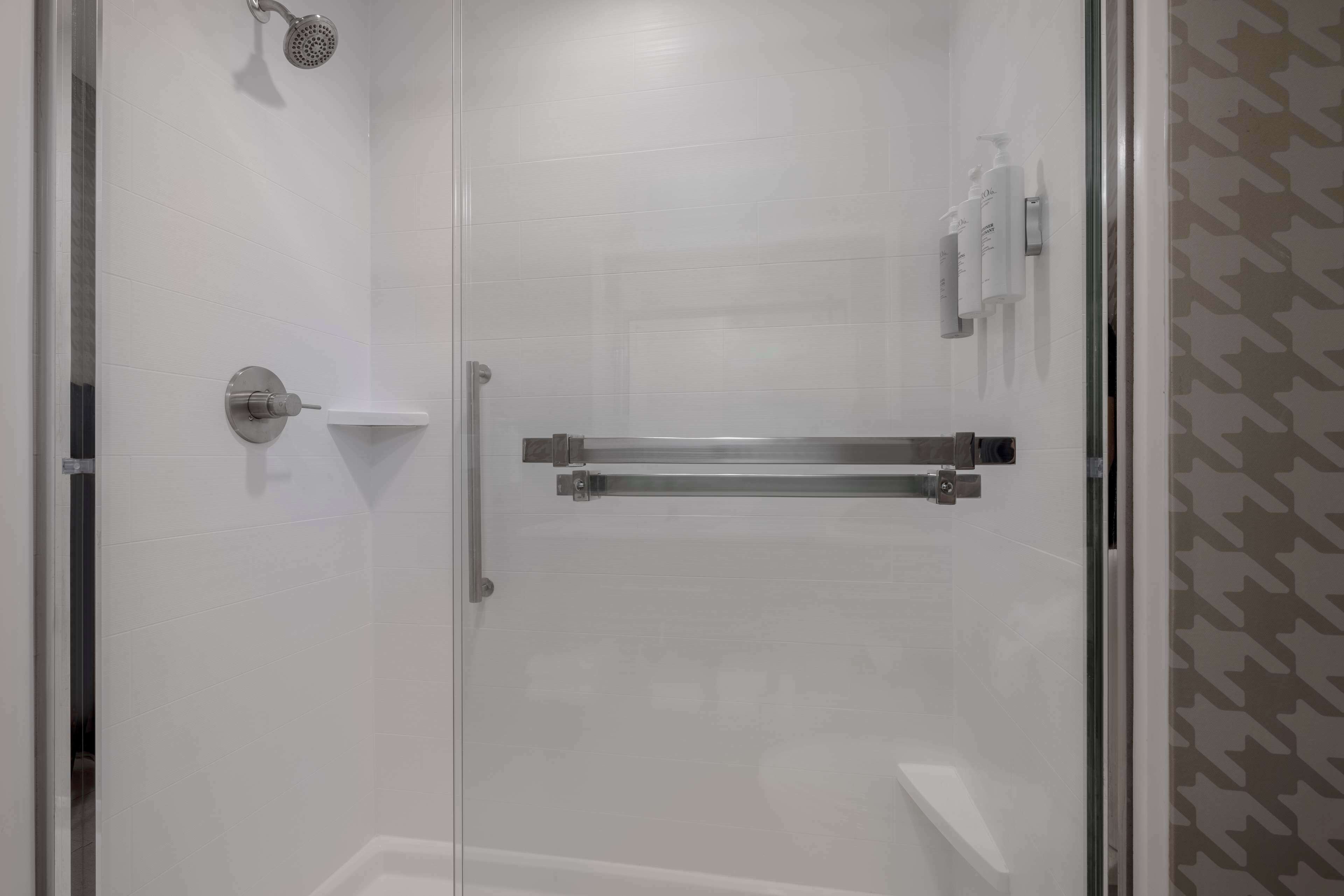 A modern shower area with a glass door, a handheld showerhead, and a towel rack.