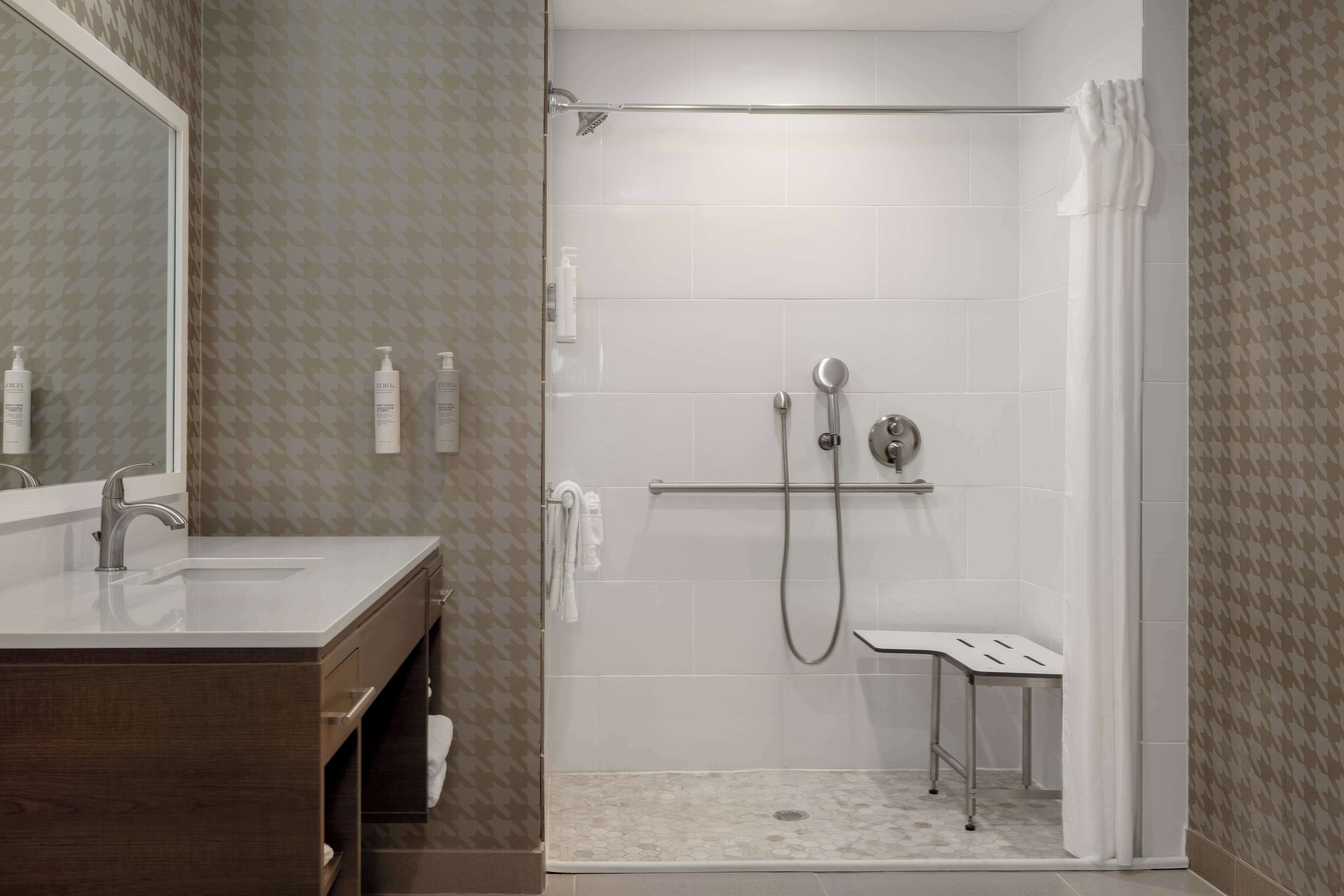 A bathroom with a shower, a vanity with a mirror, and toiletries.
