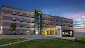 Een modern hotel met een bord waarop 'HOME 2 Suites by Hilton' staat, en een goed verlichte ingang.
