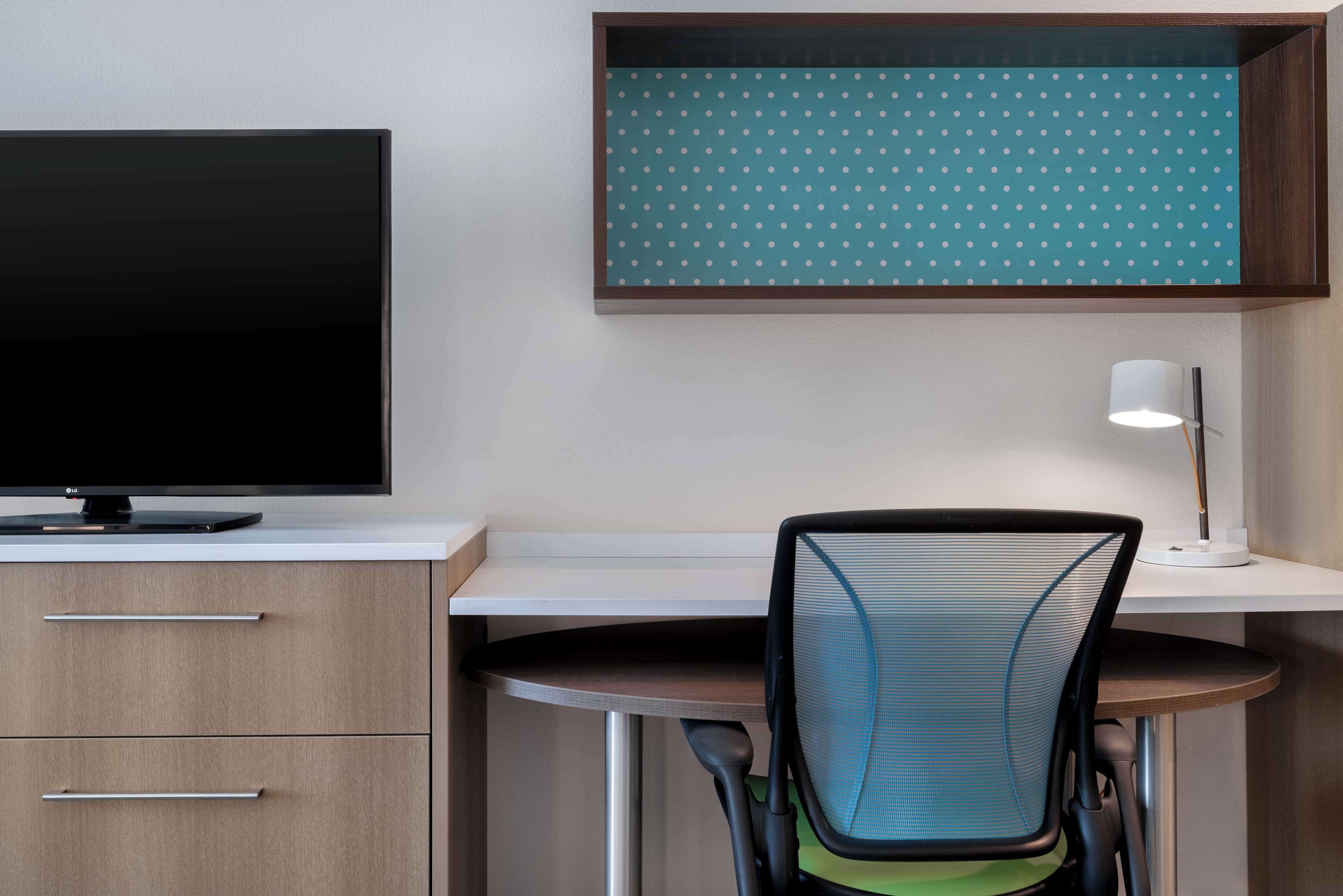 A modern office desk with a flat-screen monitor, a chair, and a lamp.