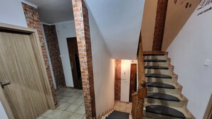 A staircase with wooden handrails and black carpeted steps, leading to a room with a door and a brick wall.