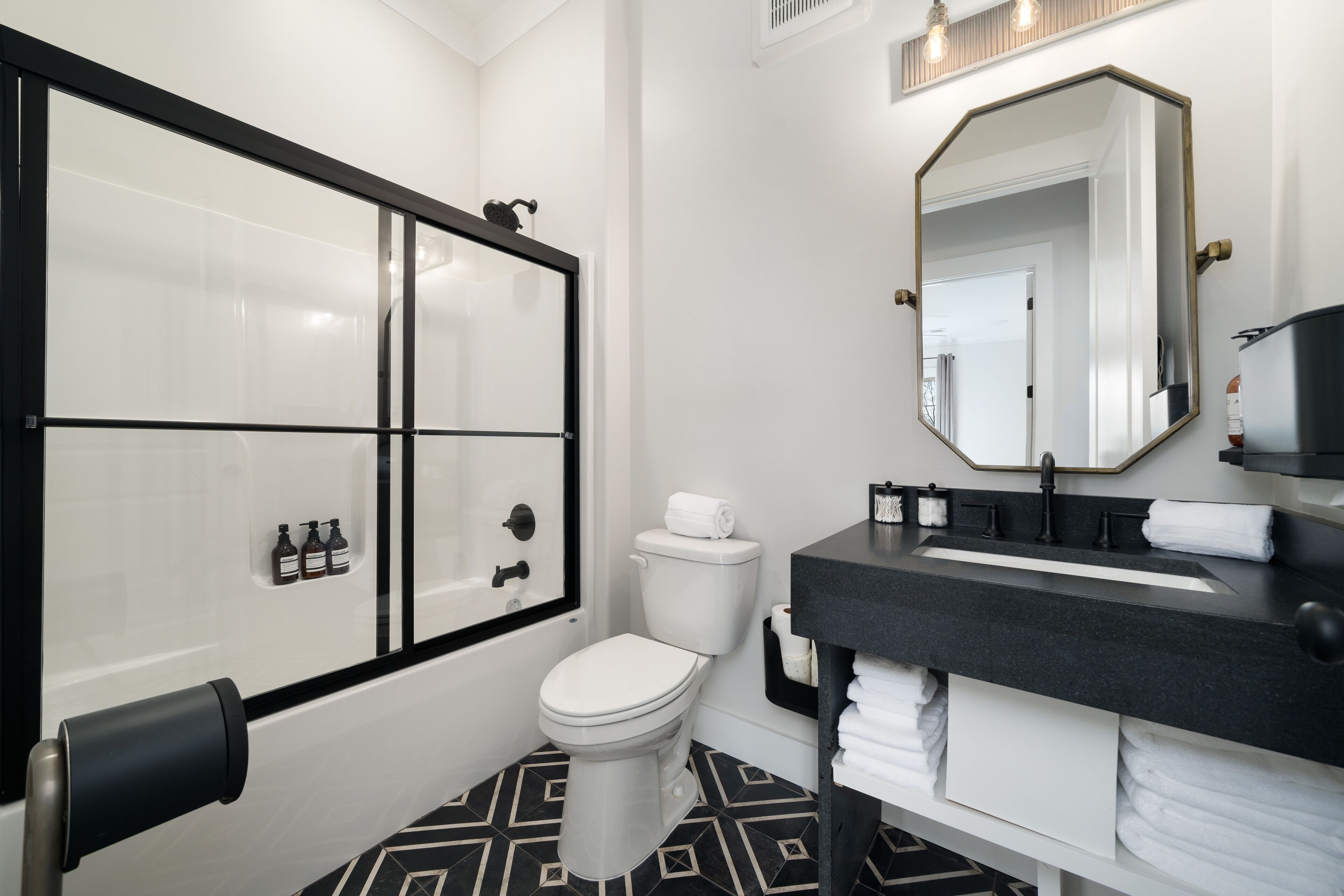 A modern bathroom with a glass-enclosed shower, a white toilet, and a black sink with a large mirror.