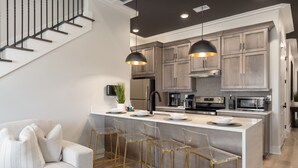 Een moderne keuken met een centraal eiland, krukken en hanglampen.