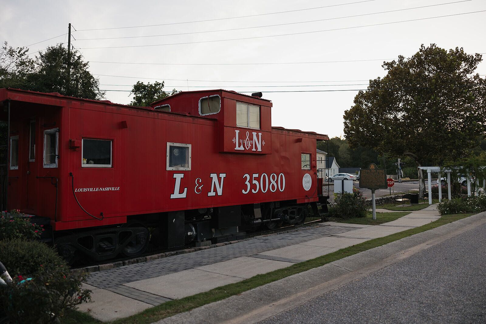 A red train car with 'L&N 35080' and 'Louisville-Nashville' written on it, parked on tracks near a road.