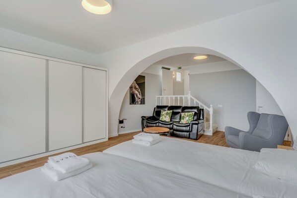 A modern bedroom with a large bed, a sofa, a chair, and a staircase leading to an upper level.