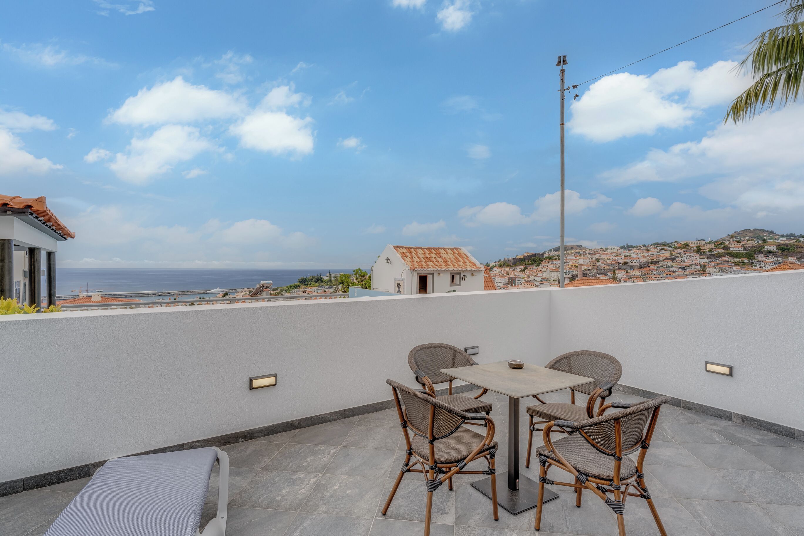 A terrace with a table and chairs, overlooking a coastal town.