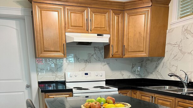 A kitchen with wooden cabinets, a white stove, a marble backsplash, and a black countertop.