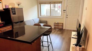 A compact kitchen with a refrigerator, a dining area with a table and chairs, a small bench, and a potted plant.
