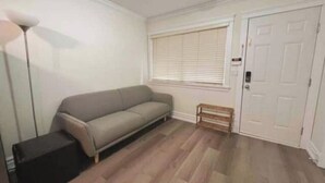 A room with a grey sofa, a small wooden bench, a white door, and a floor lamp.