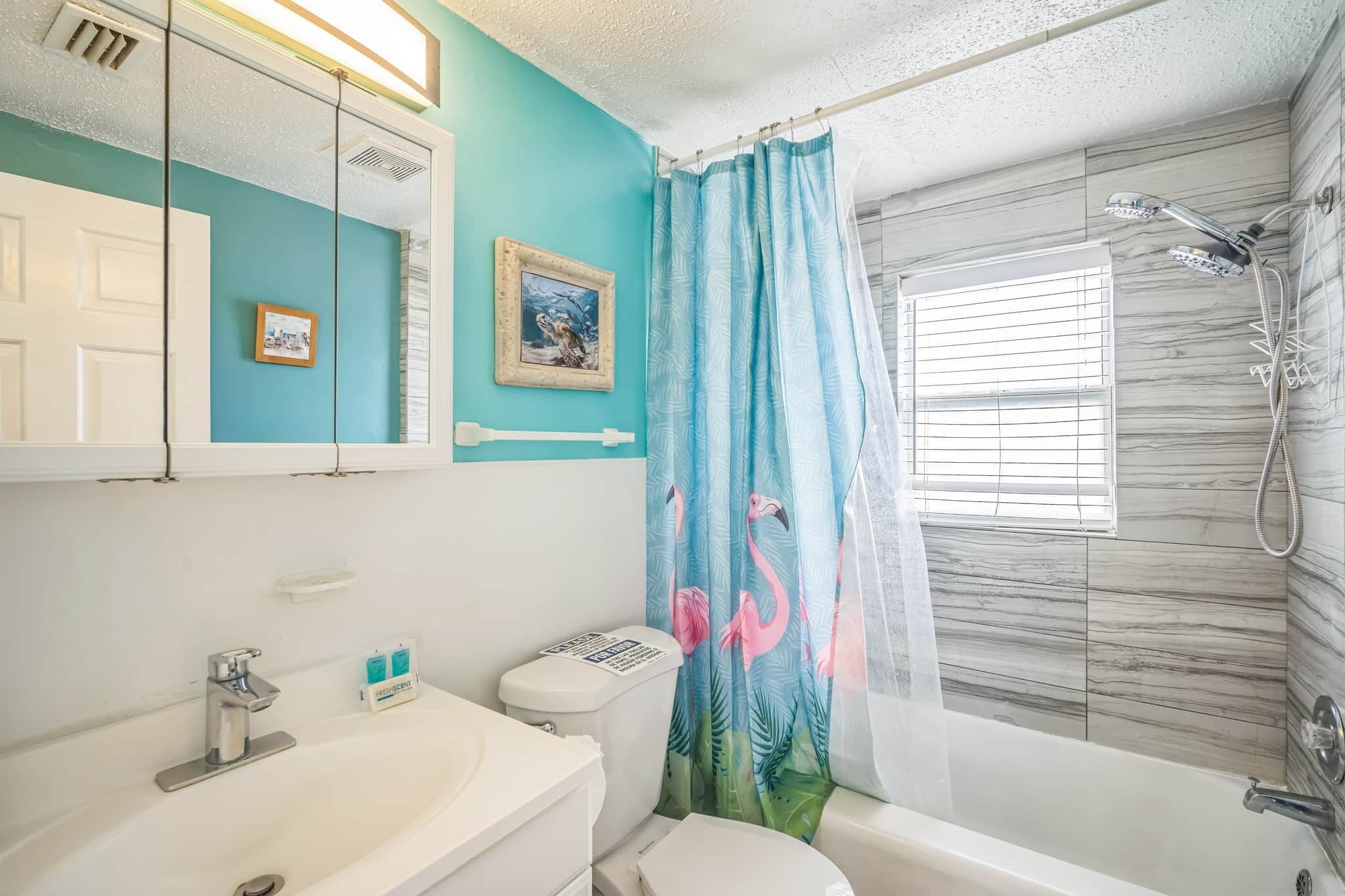 A bathroom with a white sink, toilet, and bathtub. There is a showerhead above the bathtub and a window with blinds.