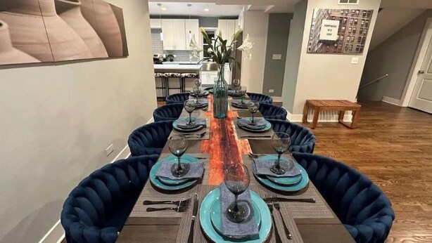 Un espace repas avec une longue table dressée pour six personnes, entourée de chaises à l’assise rembourrée de couleur bleu foncé.