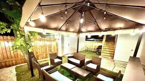 Un espace extérieur aménagé en patio, doté d’un coin salon couvert et d’une clôture en bois en arrière-plan.