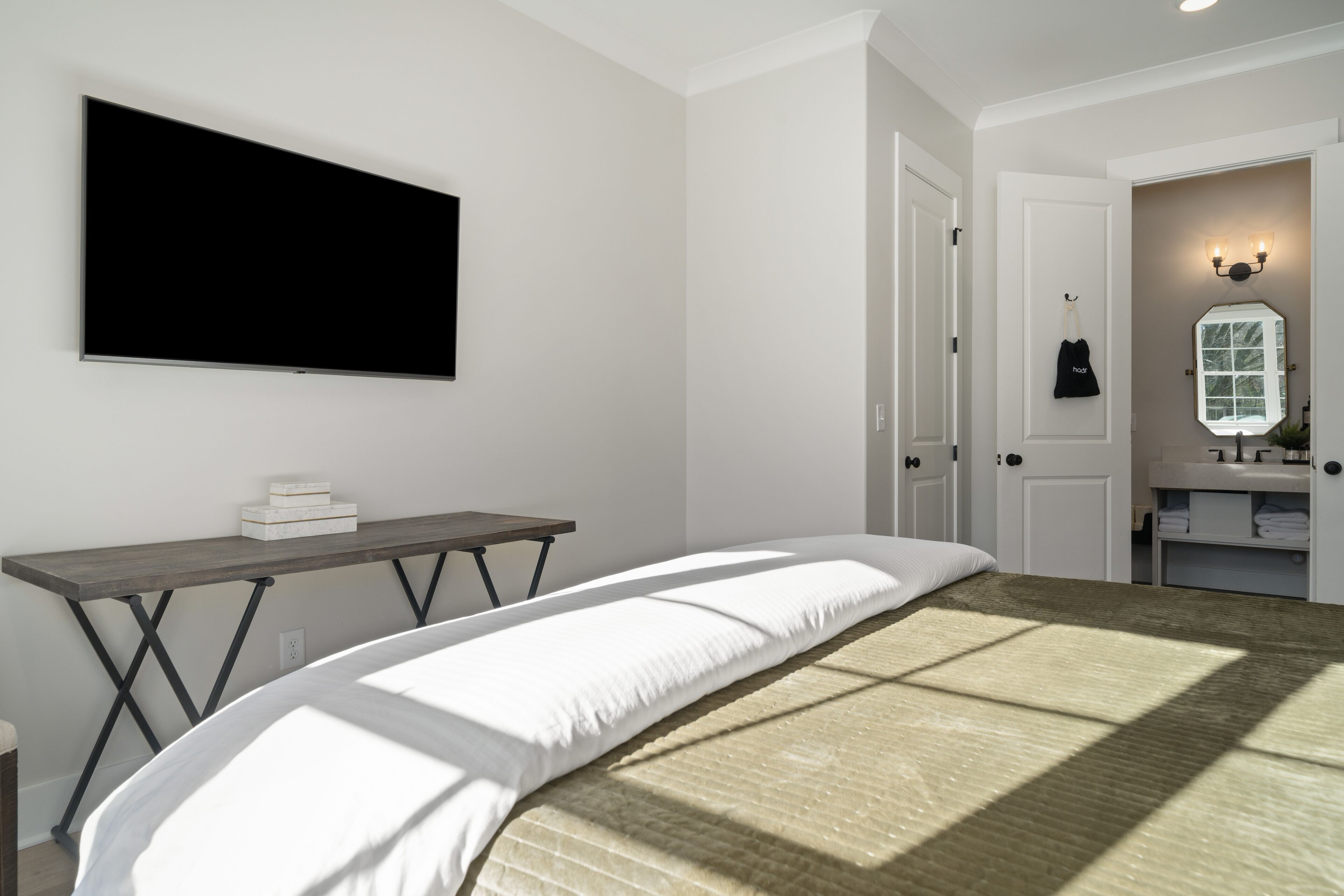Una camera da letto con un letto, una scrivania, una televisione e un bagno visibile attraverso una porta aperta.