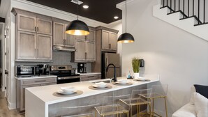 A modern kitchen with a central island, stainless steel appliances, and a staircase leading to an upper level. - 2 Bedroom Suite + Loft, Second Floor (Helena)