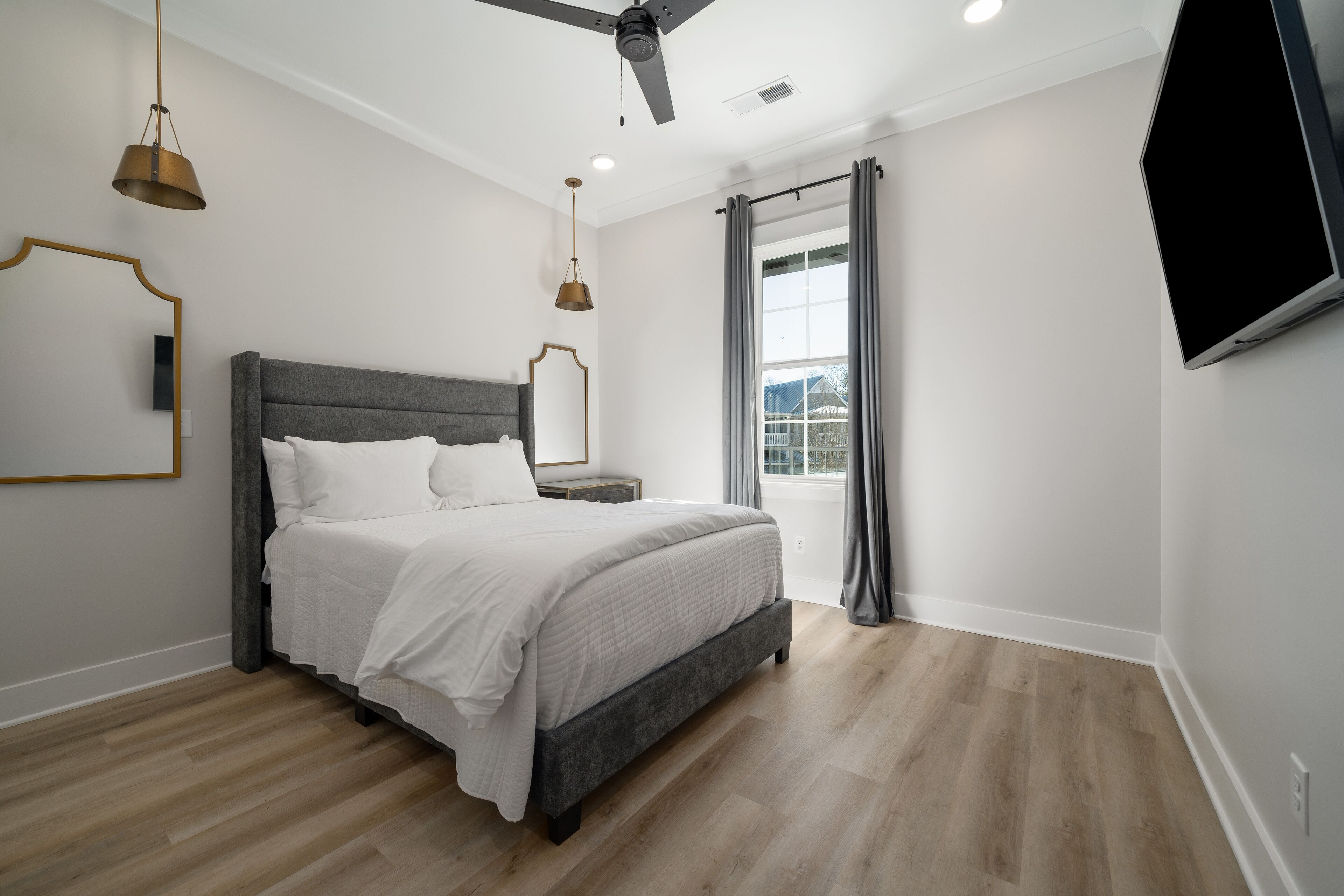 A bedroom with a bed, a ceiling fan, a TV, and a window with curtains.