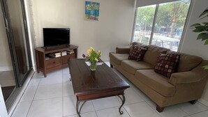 A living room with a sofa, a coffee table, a TV, and a window with a view of the outdoors. - Captain Jax (Key Largo)