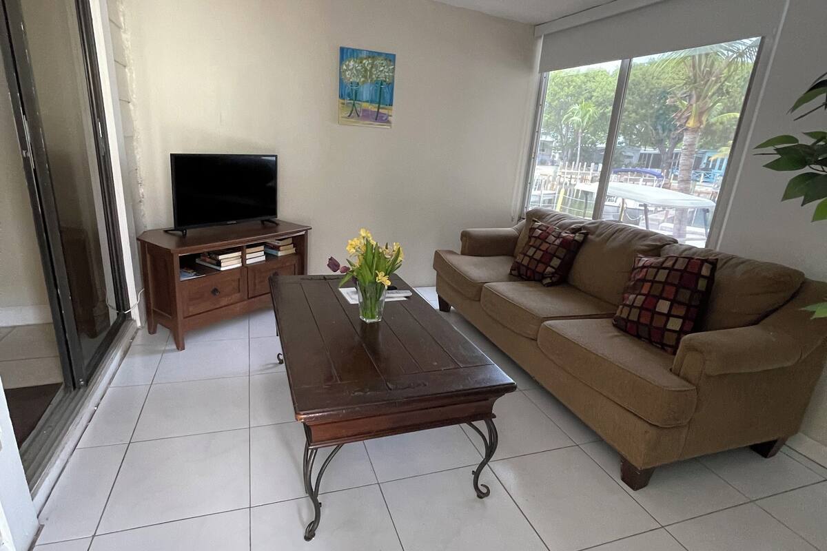 A living room with a sofa, a coffee table, a TV, and a window with a view of the outdoors.