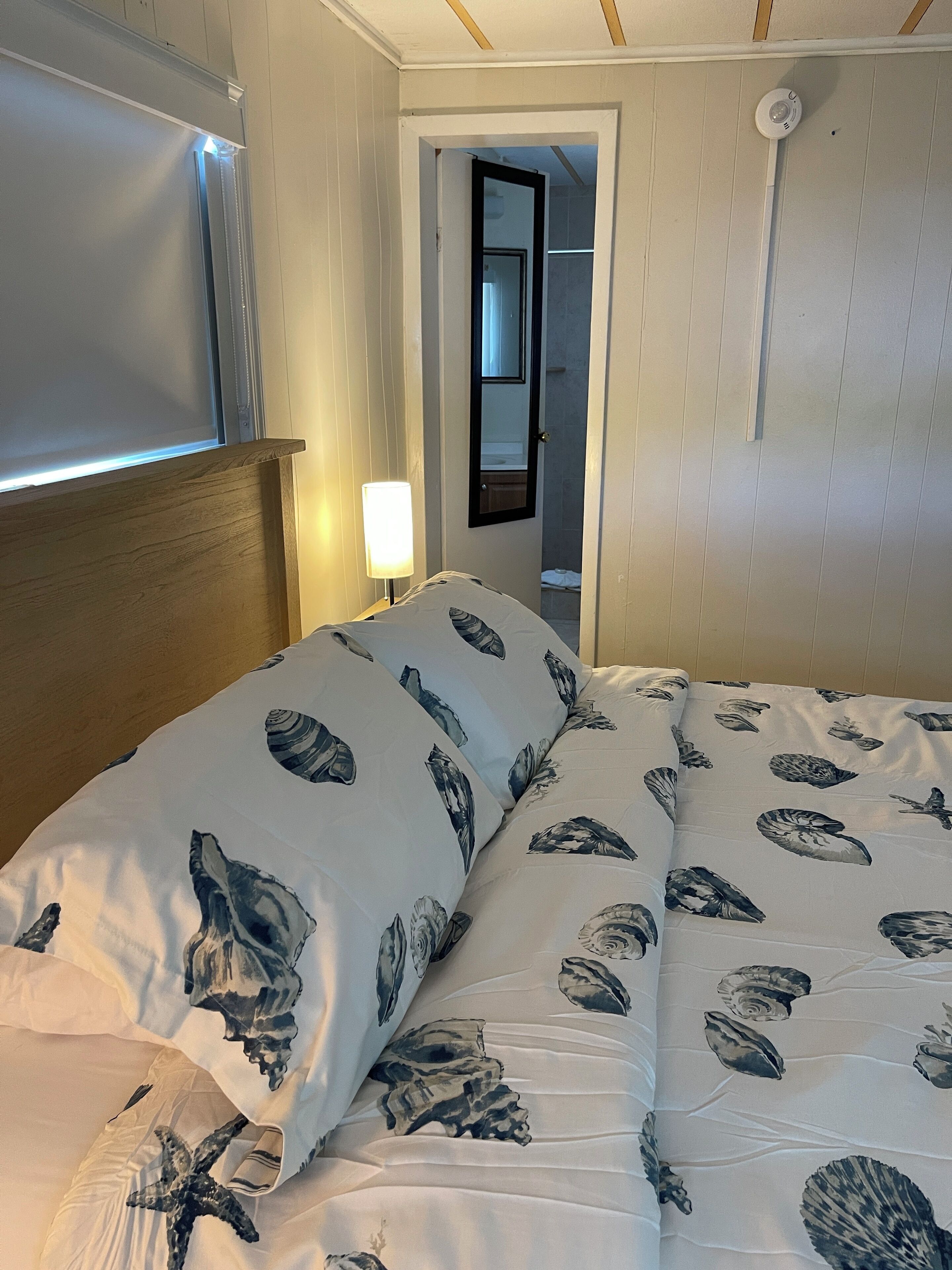 Una cama con estampado floral, una lámpara de noche y una puerta que da a un baño.