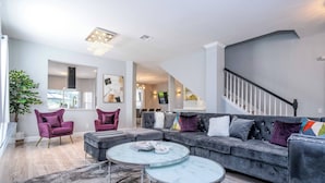 A modern living room with a sectional sofa, two armchairs, a marble coffee table, and a staircase. - Luxury Windsor Haven: 6BR Private Pool & Game Room (Kissimmee)