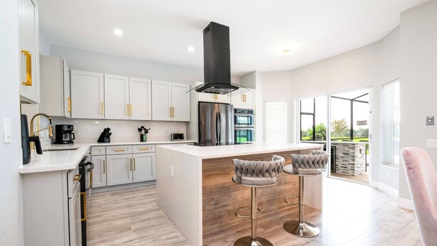 A modern kitchen with white cabinets, stainless steel appliances, and a central island with bar stools. - Luxury Windsor Haven: 6BR Private Pool & Game Room (Kissimmee)