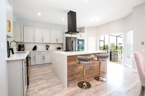 Une cuisine moderne avec des meubles blancs, des appareils en acier inoxydable et un îlot central doté de tabourets de bar.