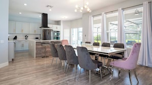 A modern kitchen with white cabinets, a stainless steel range, and a central island with bar stools. - Luxury Windsor Haven: 6BR Private Pool & Game Room (Kissimmee)