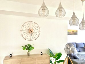 A room with a wooden cabinet, a geometric wall clock, a potted plant, a small figurine, and a standing fan.