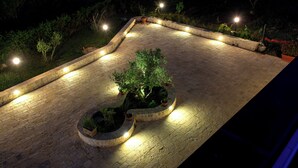 Un patio al aire libre con suelo de piedra, plantas en macetas y varias luminarias.