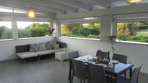 Un patio amplio con una mesa de comedor, sillas y un sofá. Grandes ventanales ofrecen vistas a zonas verdes.
