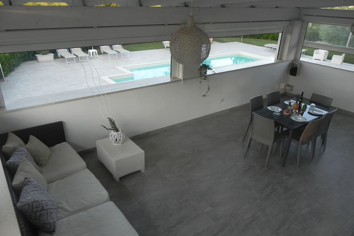 A modern living room with a sofa, a dining table, and a view of a swimming pool.