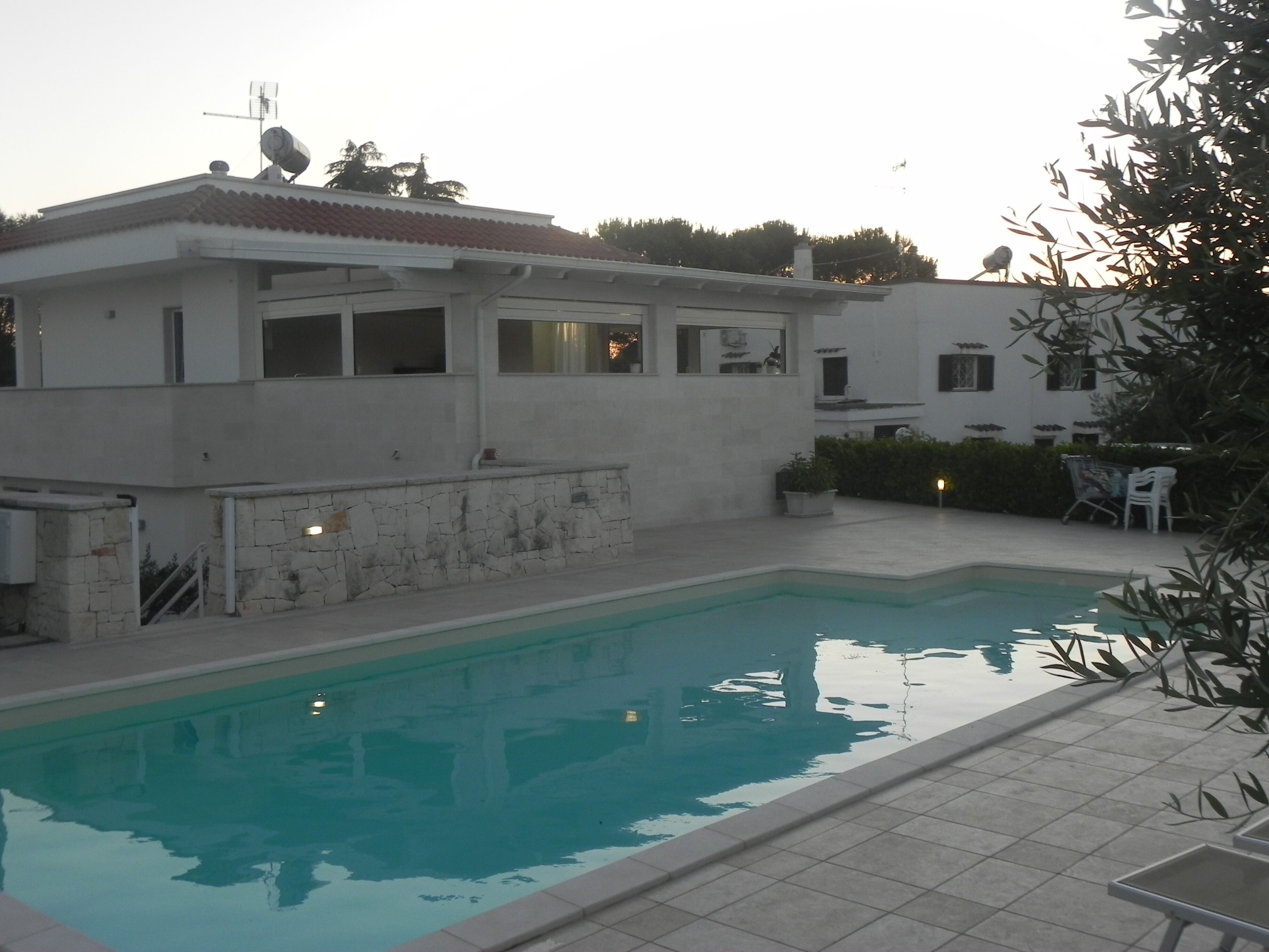 A swimming pool area with a building that has a tiled roof and a stone wall.