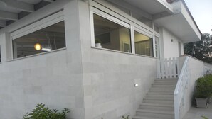Un edificio moderno con una escalera que conduce a un balcón, ventanas amplias y plantas en macetas.