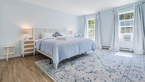 Quarto com cama, mesas de cabeceira, tapete e janela com cortinas.