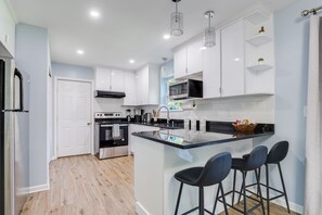 A modern kitchen with white cabinets, a stainless steel oven, a microwave, and a glass island with bar stools. - Luxury in Poconos - 3BR 3BA - Family and Pet friendly-Hot tub-Game Room-Firepit! (Albrightsville)
