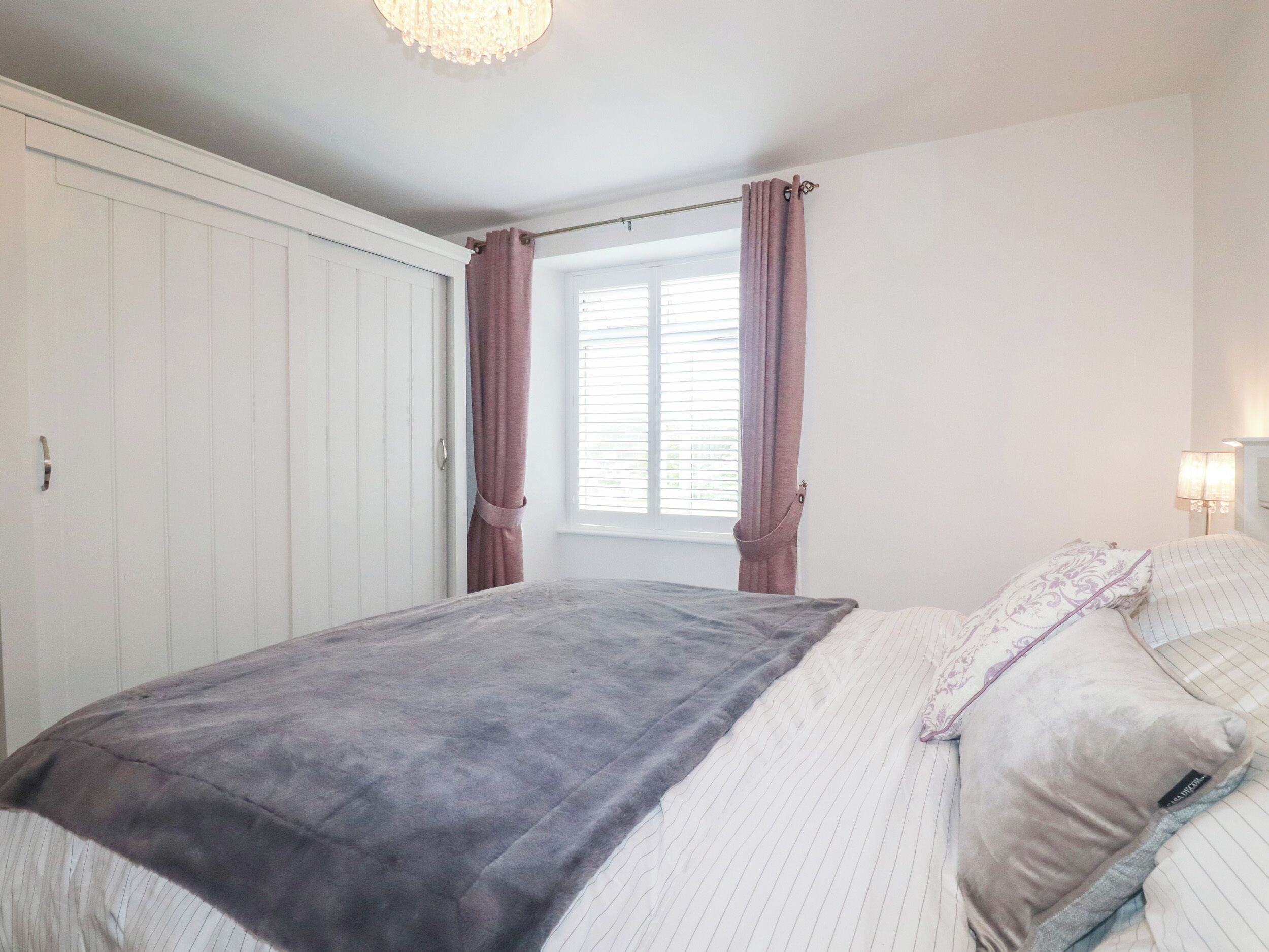 A bedroom with a bed, a window with curtains, a wardrobe, and a lamp.