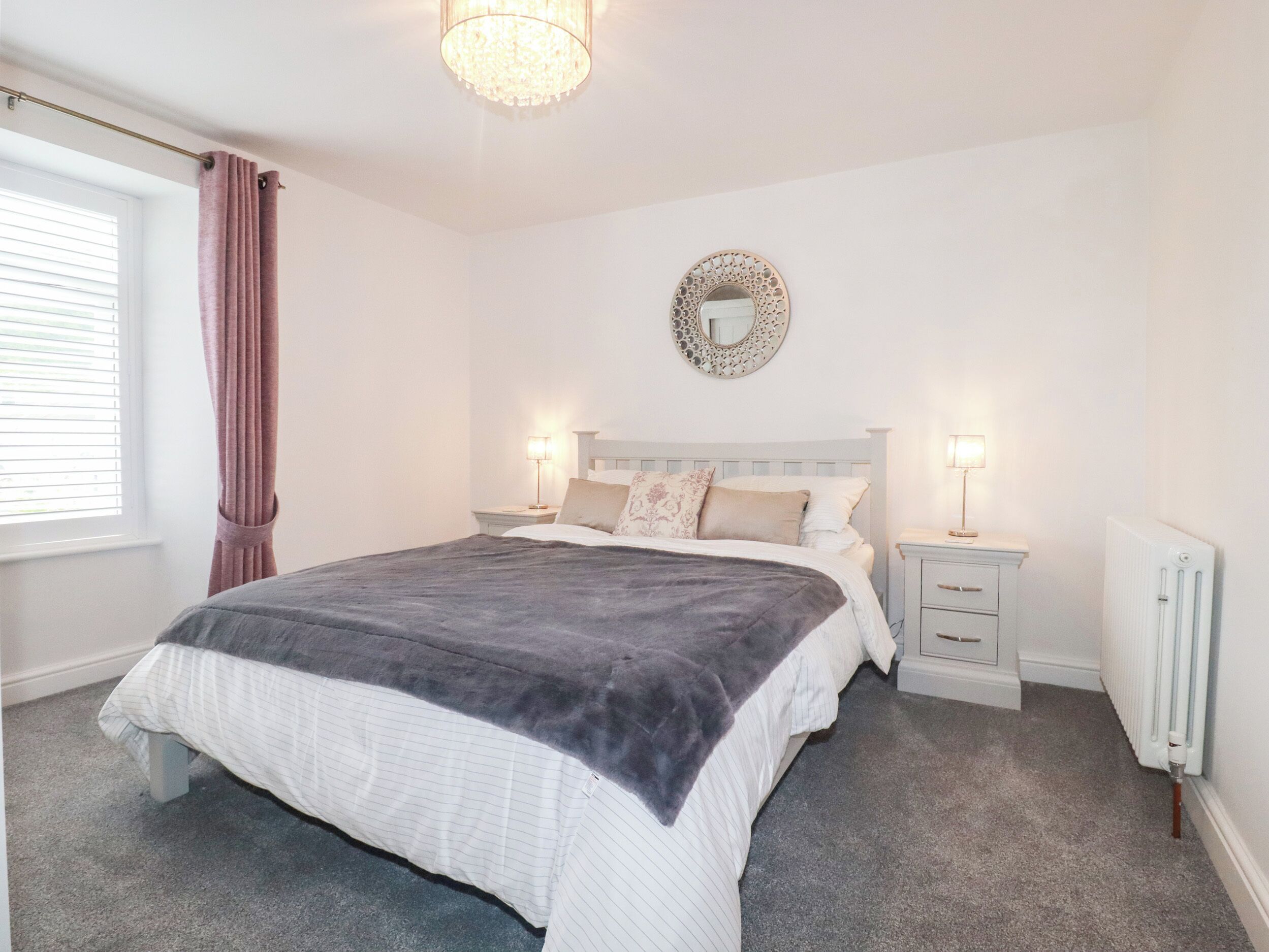 A bedroom with a bed, bedside tables, a mirror, and a radiator.