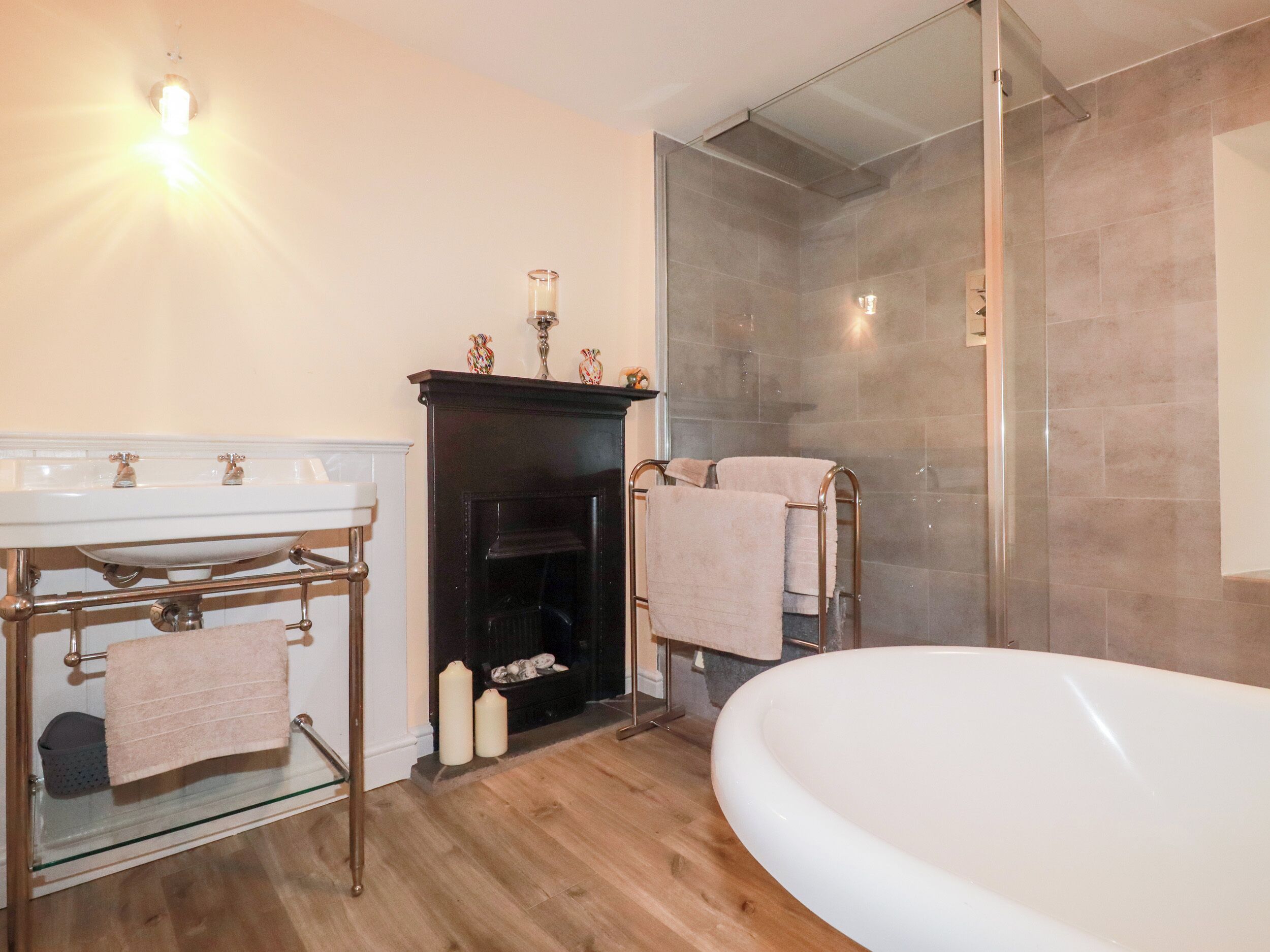 A modern bathroom with a freestanding bathtub, a glass-enclosed shower, and a fireplace with decorative vases.