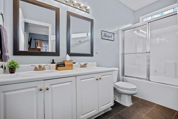 A bathroom with a double sink vanity, a toilet, and a glass-enclosed shower.