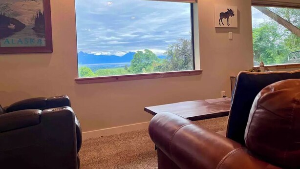 Une pièce dotée d’une grande fenêtre donnant sur un paysage montagneux, d’un fauteuil de massage, d’une petite table et d’un tableau encadré représentant un élan.