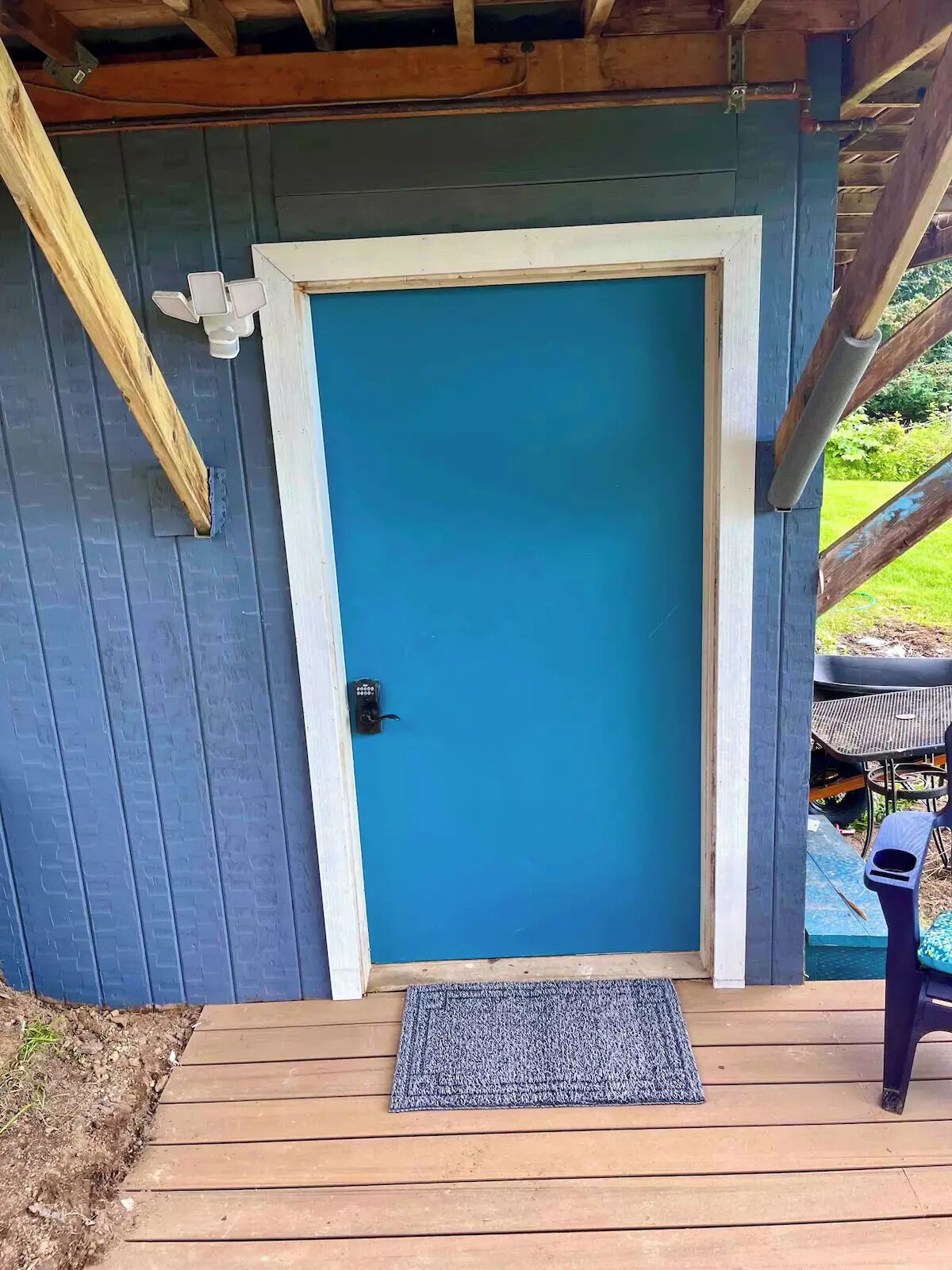 A blue door with a keypad lock, a wooden deck, and a gray doormat.