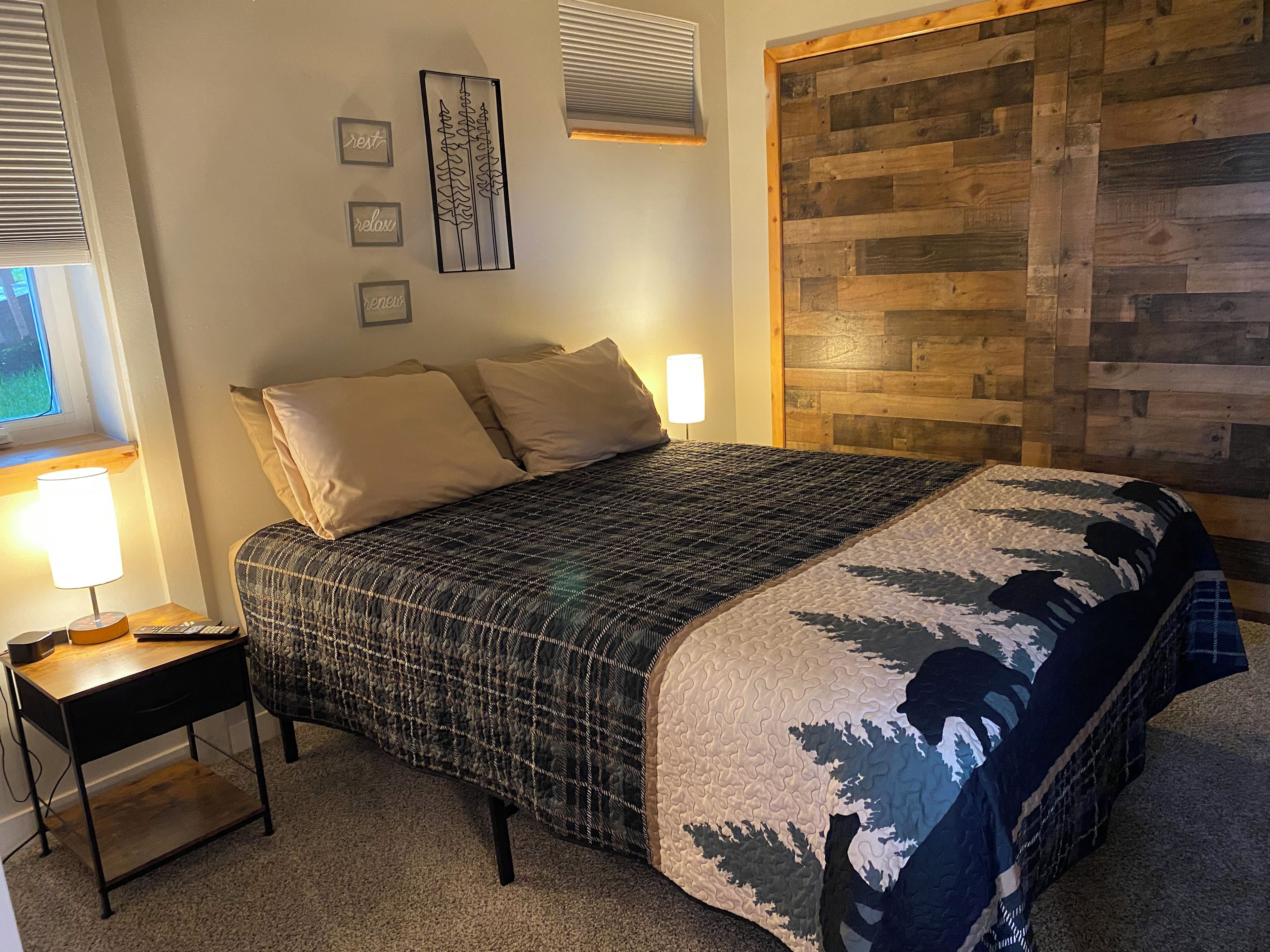 A bedroom with a bed, bedside table, lamp, and wall decor.
